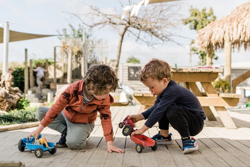 two kindergarten children playing with toy cars on a deck