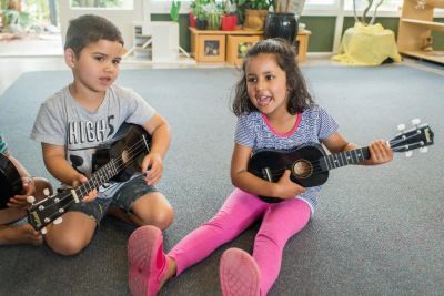 2 kids sitting on the floor playing ukelele