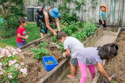 kids and woman with blue hat gardening over a raised garden bed