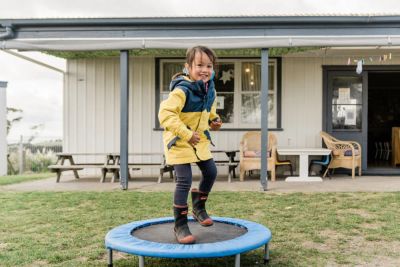 Kid jumping on a mini trampoline smiling wearing yellow jacket and gumboots